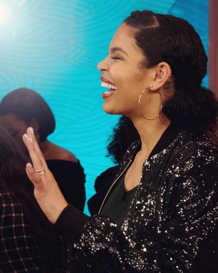 Singer Jordin Sparks laughing at a conversation in a black jacket.